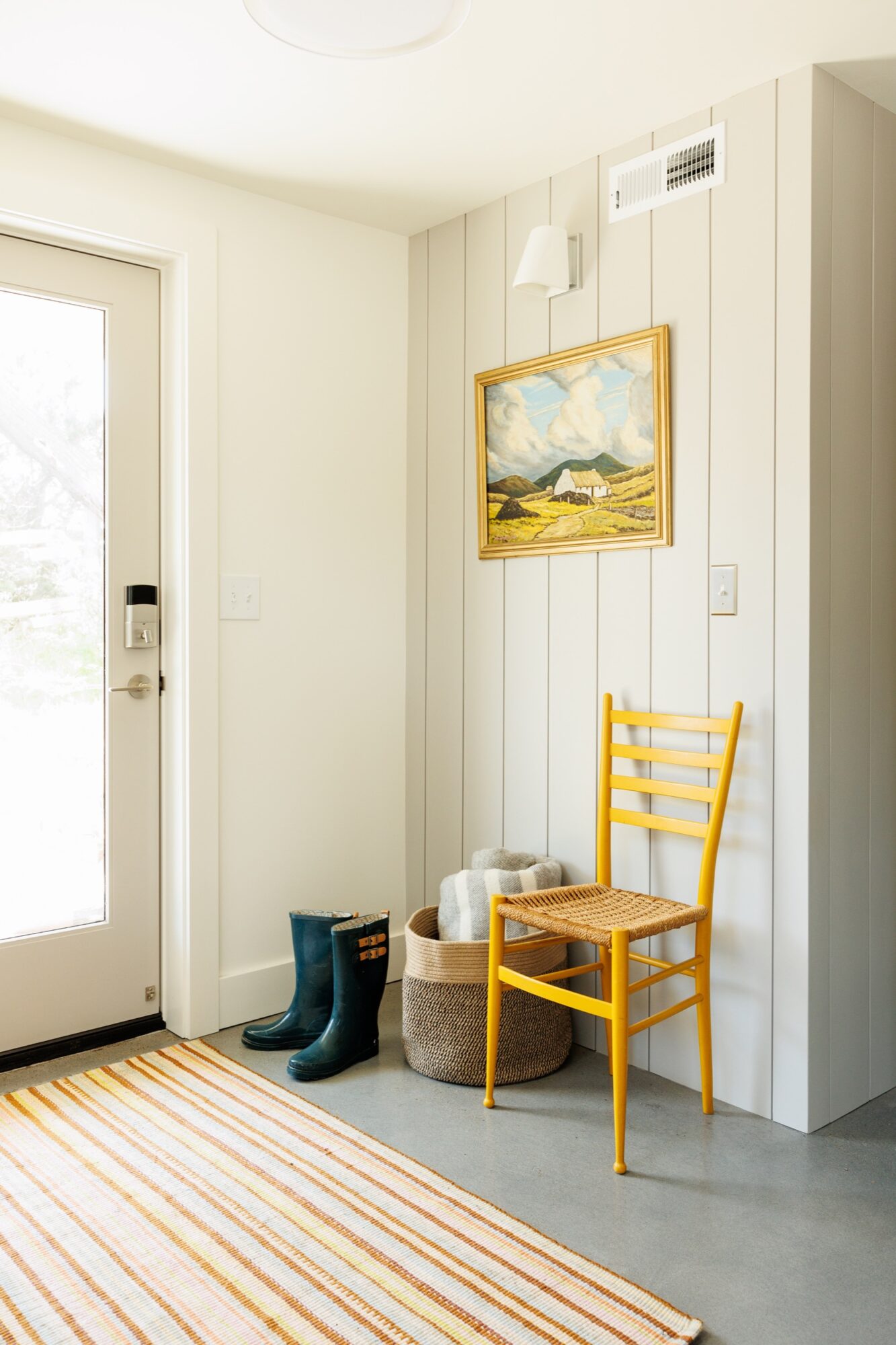 Seattle's best commercial food and hospitality photographer A bright entryway with a glass door, yellow chair, woven basket with blankets, green rain boots, striped rug, and a landscape painting on shiplap walls—captured by a Seattle commercial interior design photographer for restaurants and hotels. captured by seattle's best food and lifestyle photographer Brooke Fitts