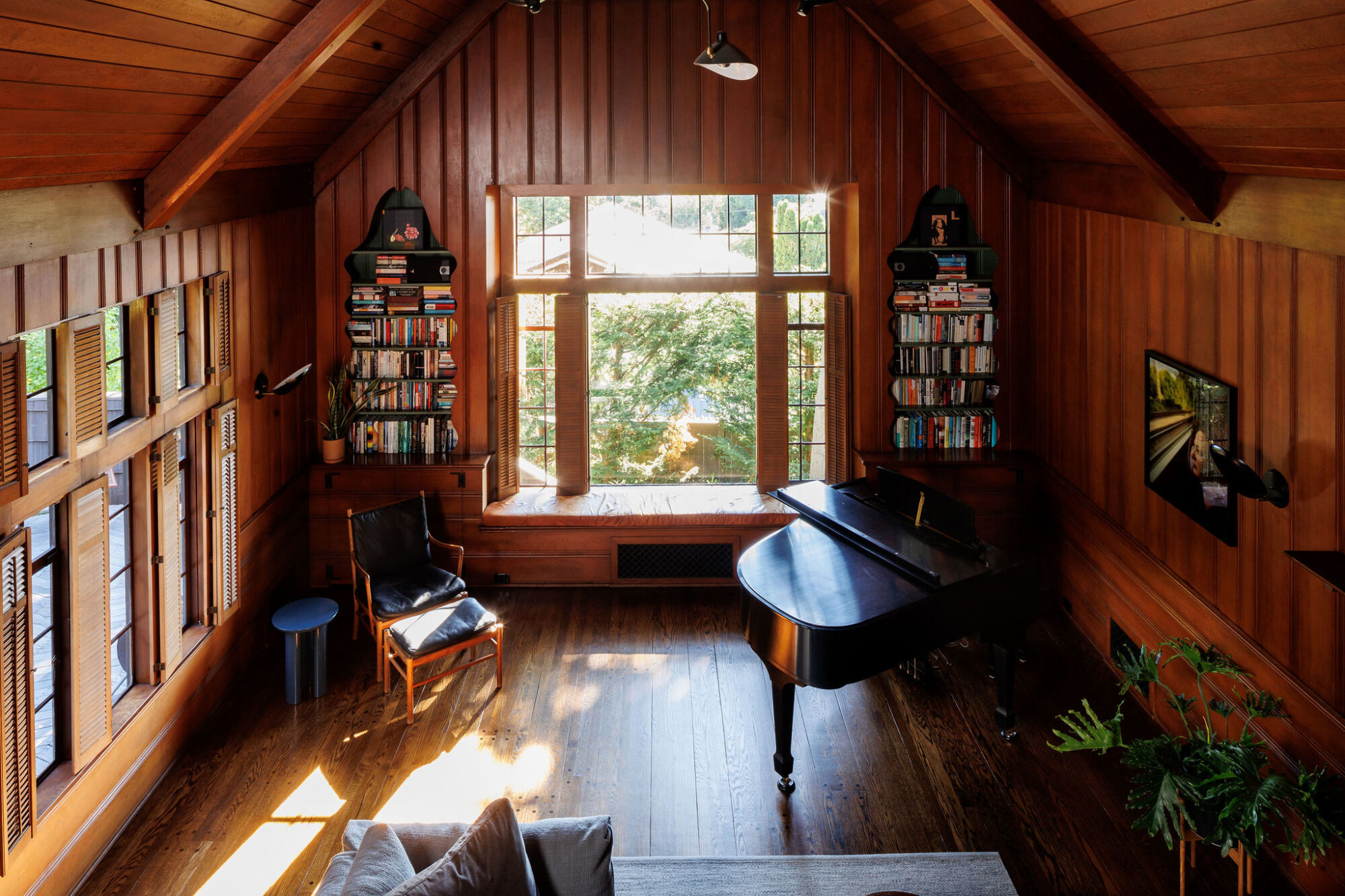Seattle's best commercial food and hospitality photographer A cozy wooden music room with a grand piano, a black chair, bookshelves flanking a large window, sunlight streaming in, and plants adding greenery to the space—captured by Seattles best commercial food lifestyle photographer. captured by seattle's best food and lifestyle photographer Brooke Fitts