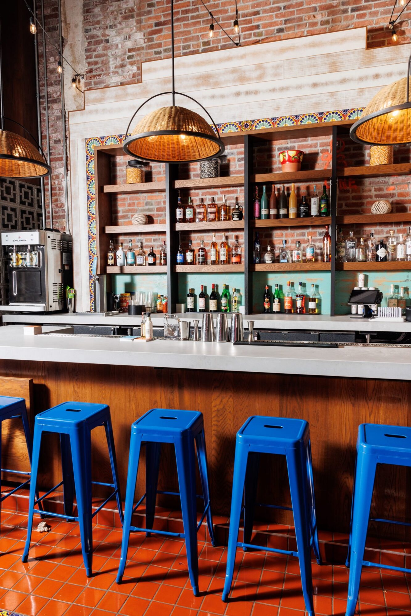 Seattle's best commercial food and hospitality photographer A modern bar with a white countertop, four bright blue metal stools, and shelves stocked with bottles and glassware. Captured by Seattles best commercial food lifestyle photographer, the brick walls and warm lighting create a cozy atmosphere. captured by seattle's best food and lifestyle photographer Brooke Fitts