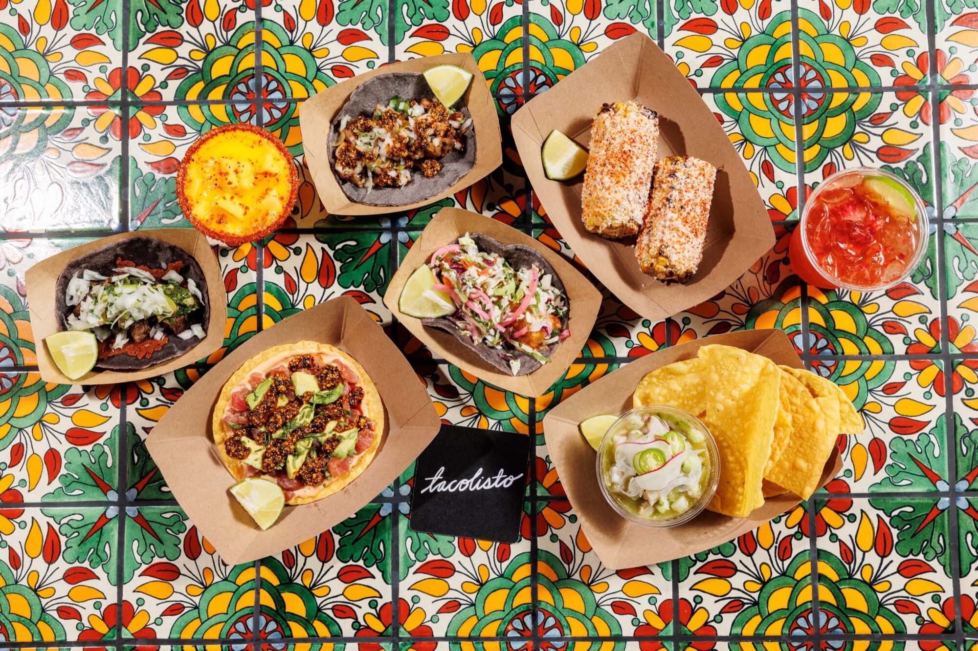 Seattle's best commercial food and hospitality photographer An overhead view of assorted Mexican dishes—tacos, corn on the cob, ceviche, nachos, a grilled dish, and two drinks—captured by Seattles best commercial food lifestyle photographer on a colorful tiled table. captured by seattle's best food and lifestyle photographer Brooke Fitts