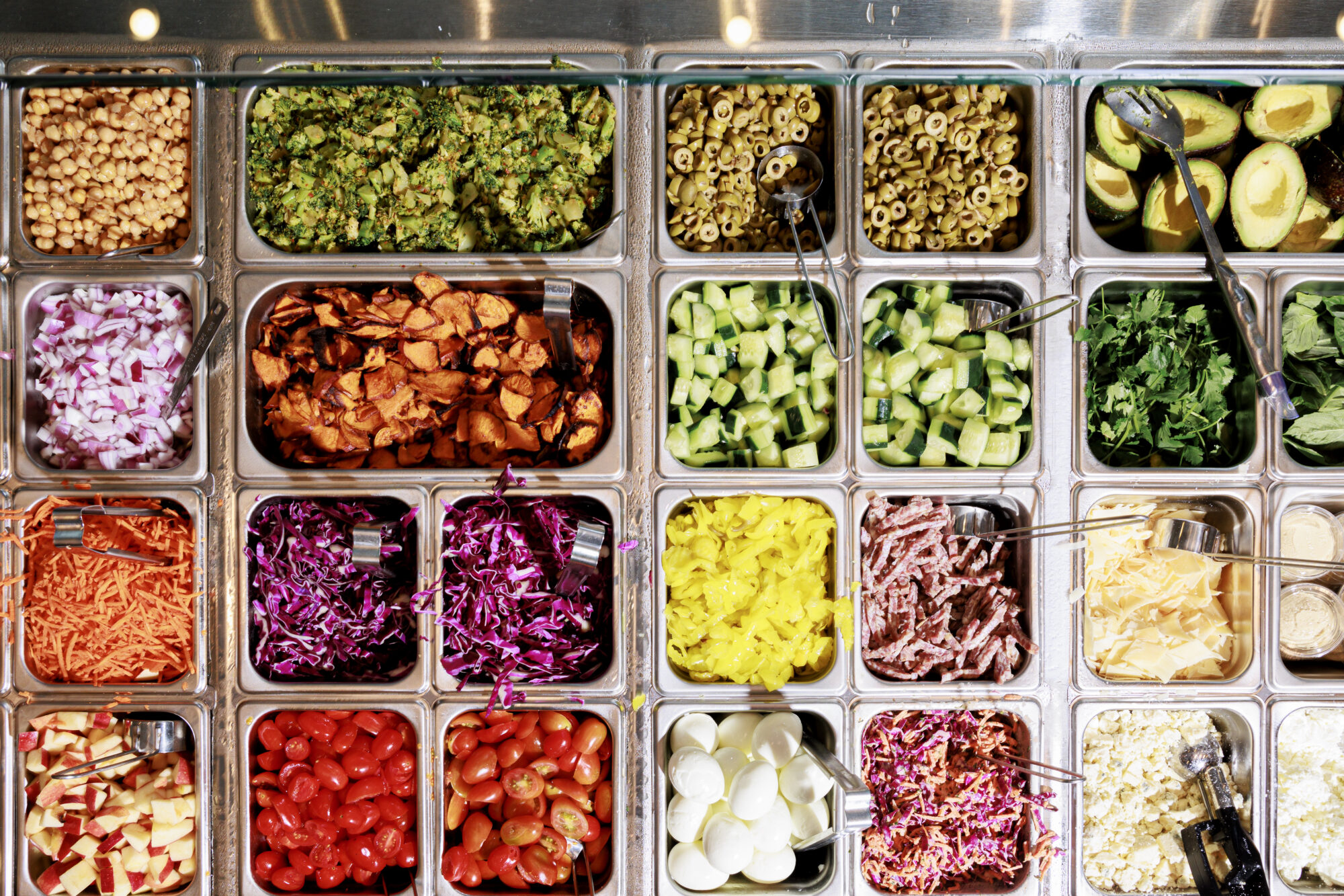 Seattle's best commercial food and hospitality photographer A salad bar with trays of various fresh ingredients, beautifully captured by Seattles best commercial food lifestyle photographer, features chopped vegetables, sliced eggs, olives, greens, shredded carrots, cherry tomatoes, and other colorful toppings. captured by seattle's best food and lifestyle photographer Brooke Fitts