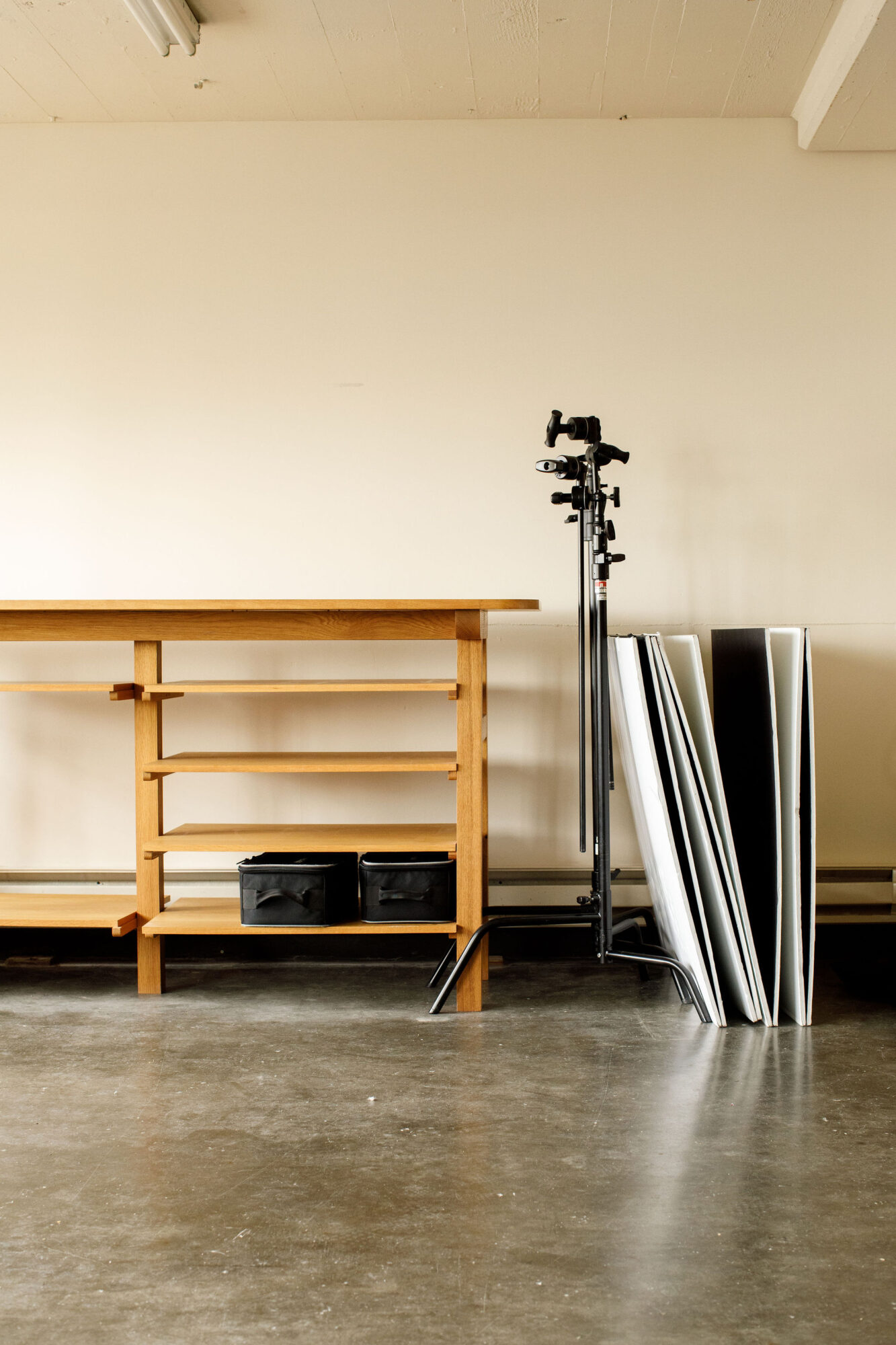 Seattle's best commercial food and hospitality photographer A wooden table with open shelves stands on a concrete floor beside two black storage boxes, several stacked boards, and two metal tripod stands—a scene captured by Seattles best commercial food lifestyle photographer in a minimalist, well-lit room. captured by seattle's best food and lifestyle photographer Brooke Fitts