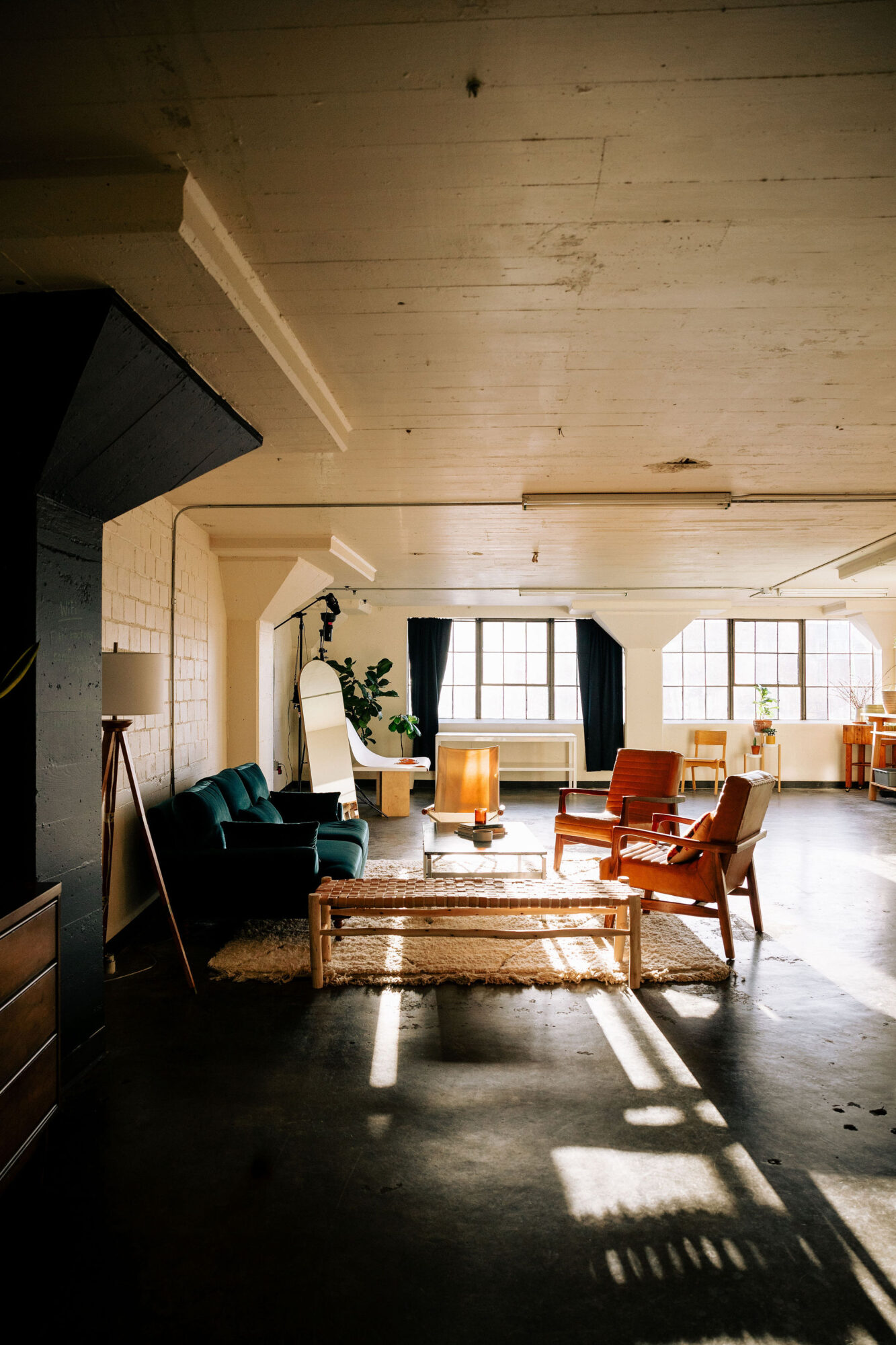 Seattle's best commercial food and hospitality photographer A spacious, sunlit living room with large windows and mid-century modern furniture is captured by Seattles best commercial food lifestyle photographer. A green sofa, wooden chairs, coffee table, rug, and potted plants bask in the warm sunlight. captured by seattle's best food and lifestyle photographer Brooke Fitts