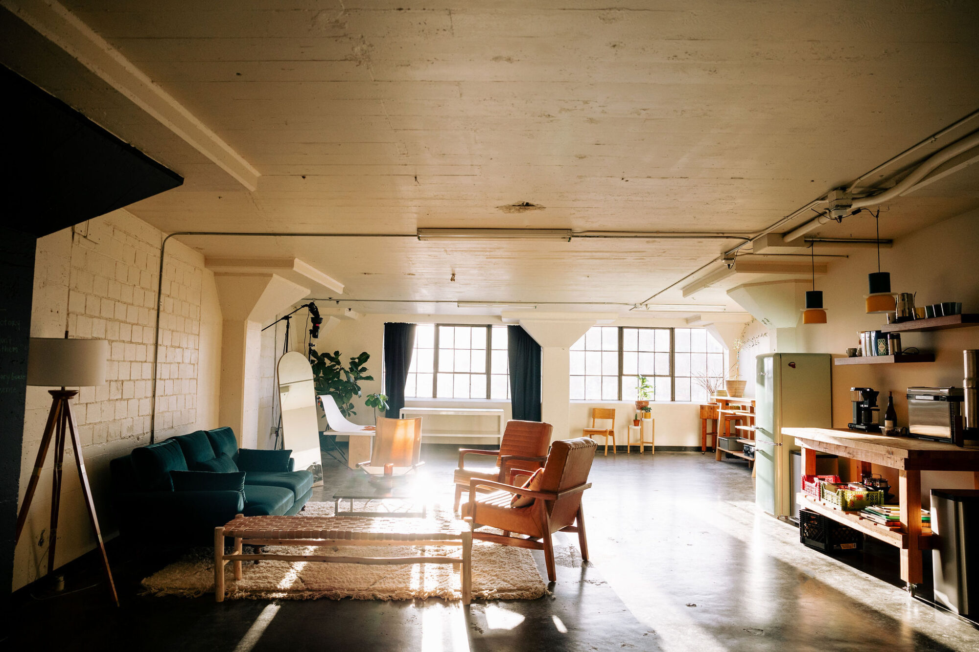 Seattle's best commercial food and hospitality photographer Sunlit loft apartment with a green sofa, armchairs, a coffee table, and a cozy rug. Captured by Seattles best commercial food lifestyle photographer, the space features large windows, kitchen shelves, and vibrant plants and decor throughout. captured by seattle's best food and lifestyle photographer Brooke Fitts