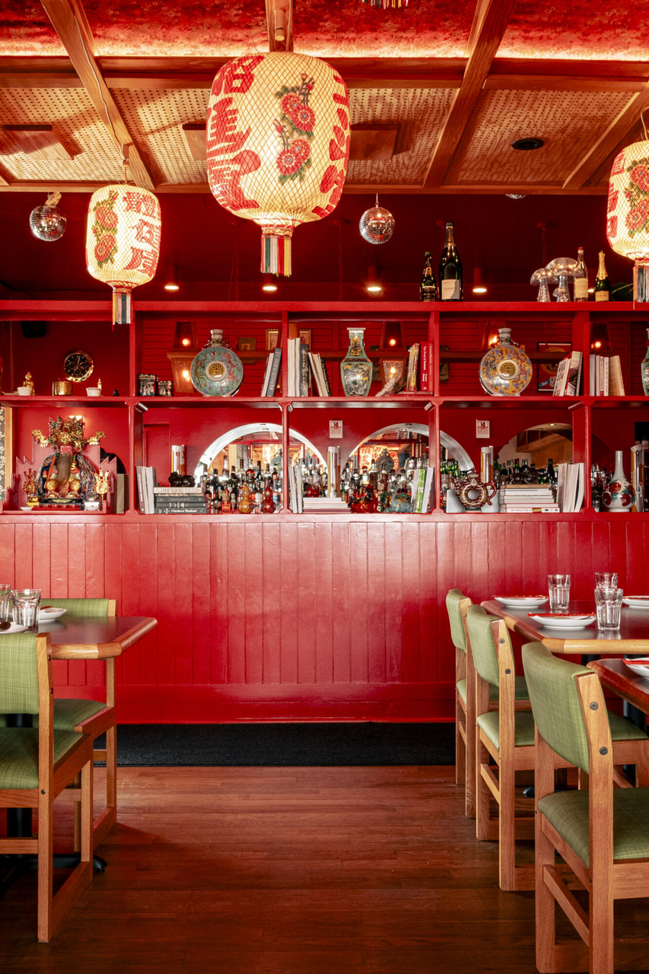 Seattle's best commercial food and hospitality photographer A vibrant restaurant interior by Seattles best commercial food lifestyle photographer, with red walls, shelves displaying vases and bottles, and large red lanterns. Green chairs and wooden tables are set for dining on a polished wood floor. captured by seattle's best food and lifestyle photographer Brooke Fitts