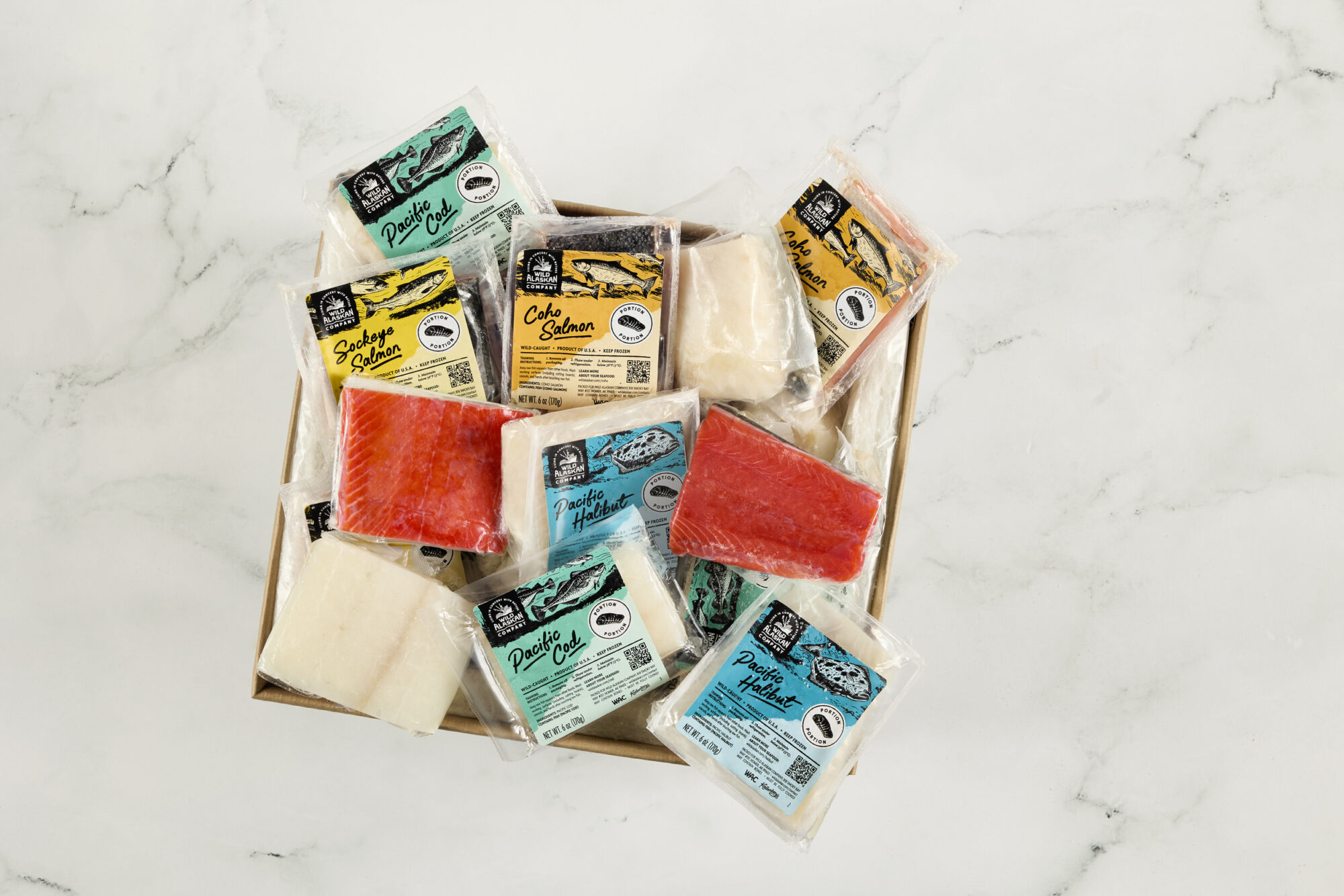 Seattle's best commercial food and hospitality photographer A box of assorted vacuum-sealed fish fillets, styled by Seattles best commercial food lifestyle photographer, includes red and white varieties like salmon and halibut, each labeled and arranged on a pristine white marble surface. captured by seattle's best food and lifestyle photographer Brooke Fitts