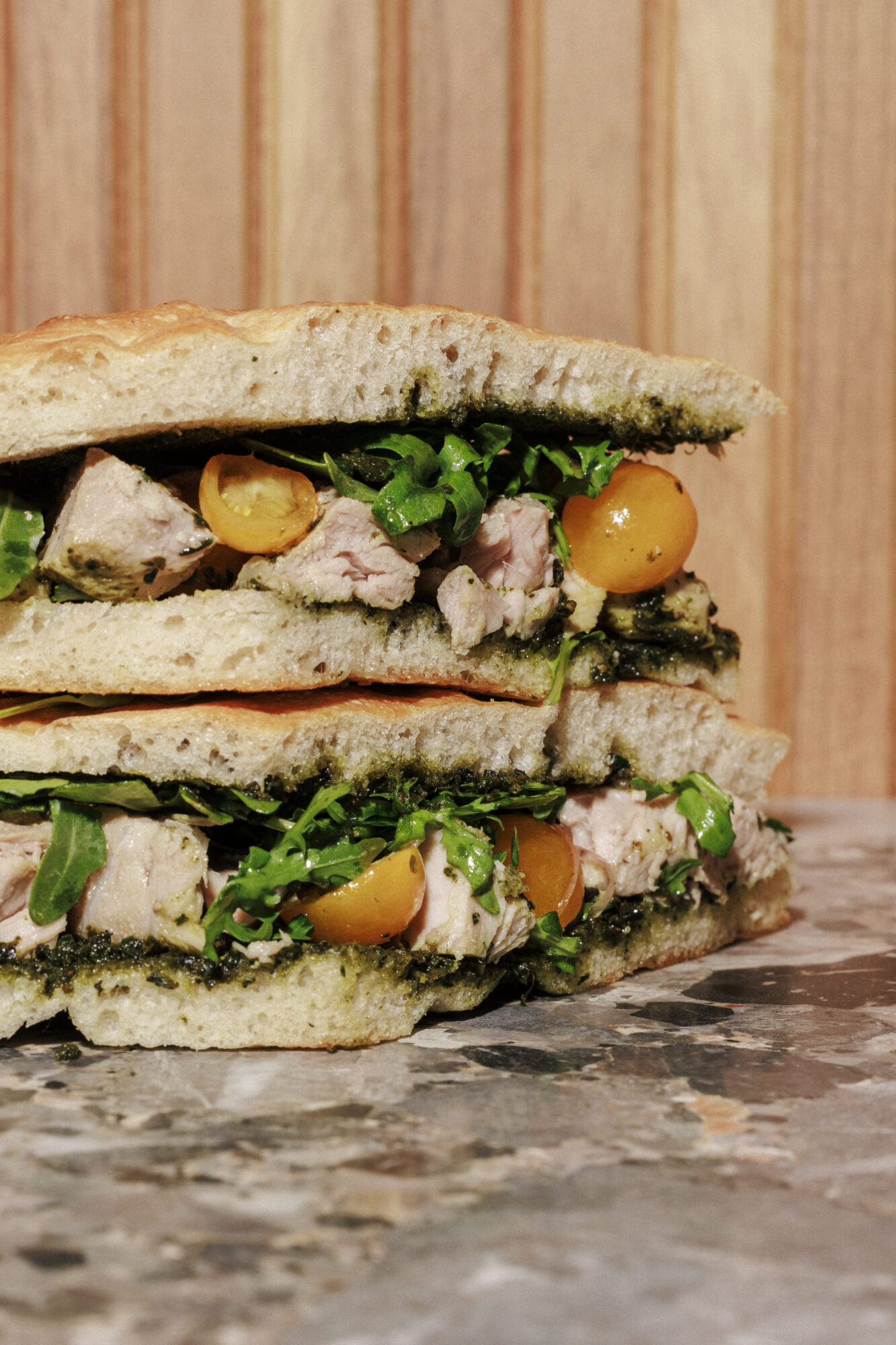 Delicious multi-layered sandwich with chicken, arugula, and pesto on rustic bread served on a marble countertop