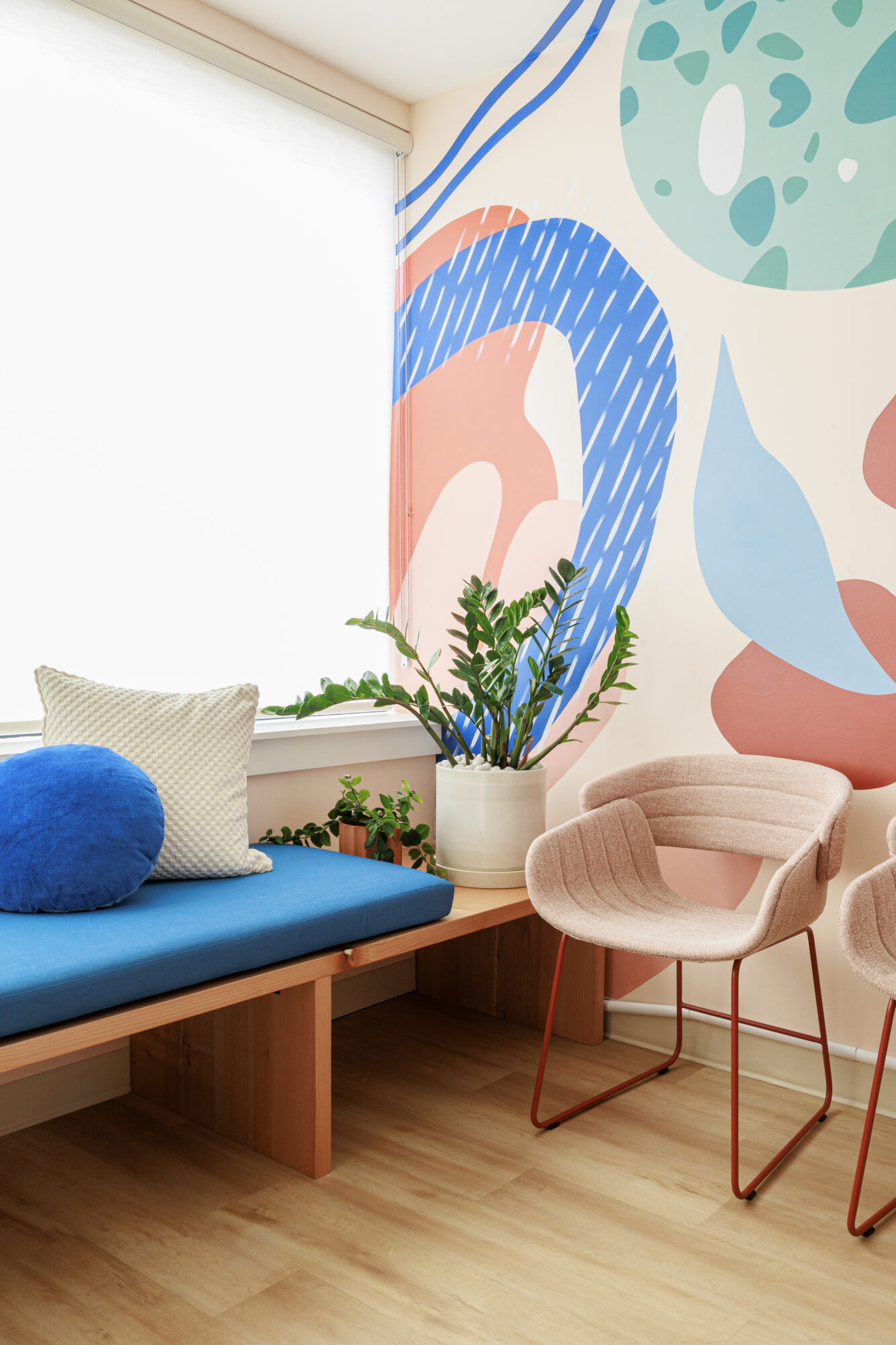 Seattle's best commercial food and hospitality photographer A bright, modern room with a blue cushioned bench, white and blue pillows, and a colorful mural—captured by Seattles best commercial food lifestyle photographer. Sunlight pours through a large window onto pink chairs and light wood floors. captured by seattle's best food and lifestyle photographer Brooke Fitts