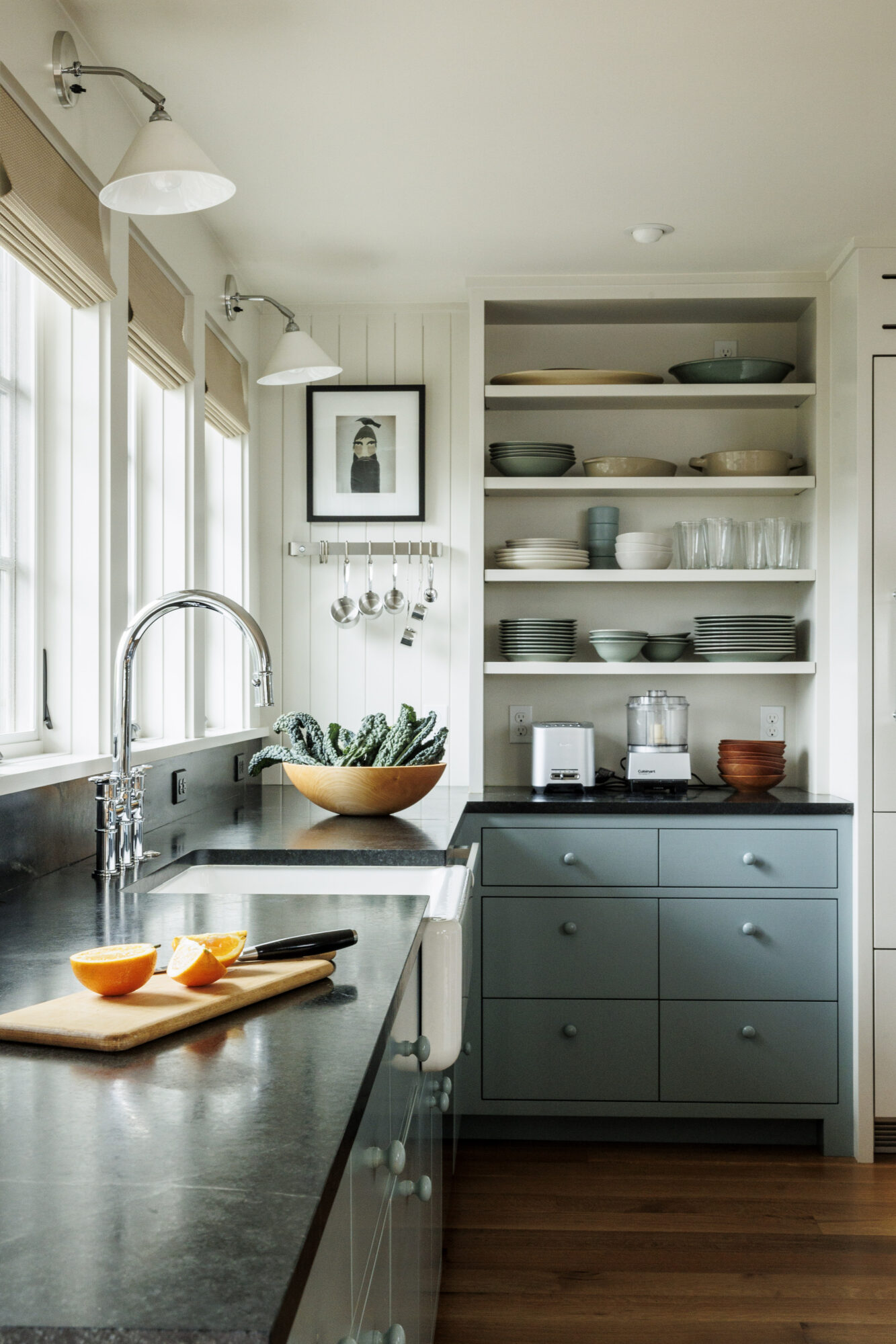 Seattle's best commercial food and hospitality photographer A bright, modern kitchen with black countertops, blue-gray cabinets, open shelves with dishes, and sunlight streaming in—captured by Seattles best commercial food lifestyle photographer. Oranges sit on a cutting board beside a wooden bowl of cucumbers. captured by seattle's best food and lifestyle photographer Brooke Fitts