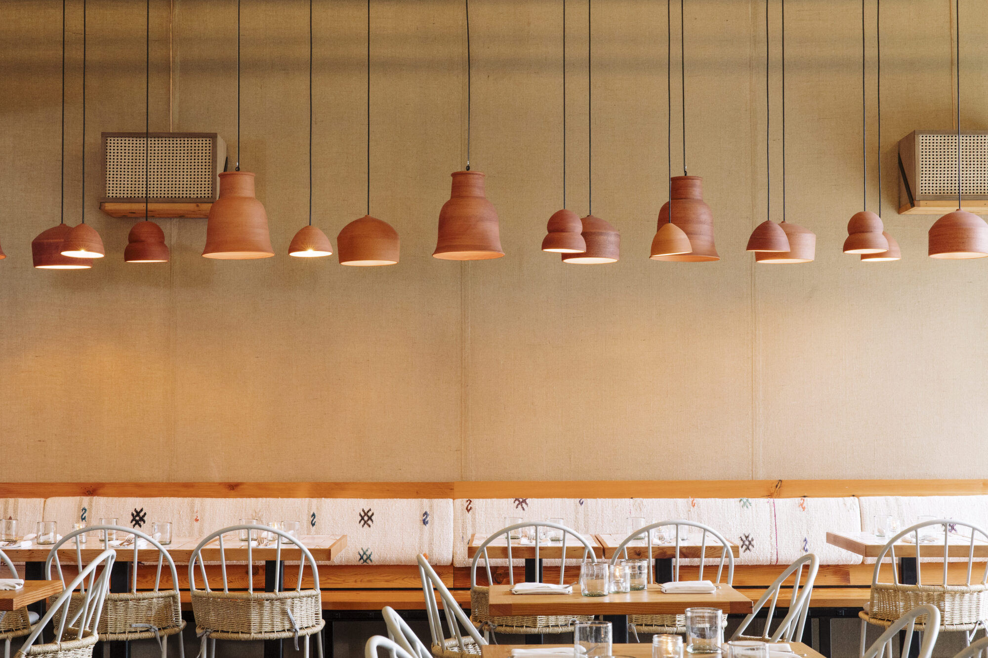 Seattle's best commercial food and hospitality photographer A row of terracotta pendant lights hangs above wooden tables and metal chairs in a cozy, minimalist restaurant—captured by a Seattle commercial interior design photographer for restaurants and hotels. captured by seattle's best food and lifestyle photographer Brooke Fitts