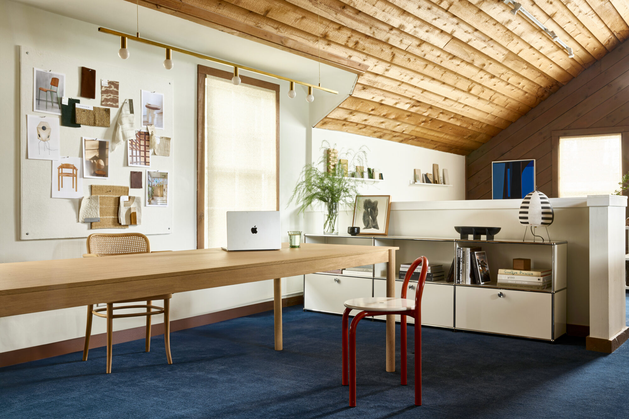 Seattle's best commercial interiors and hospitality photographer A modern home office with a wooden ceiling, a long desk, blue carpet, wall art, books, plants, and decor is captured in natural light—styled by a Seattle commercial interior design photographer for restaurants and hotels. captured by seattle's best food and lifestyle photographer Brooke Fitts