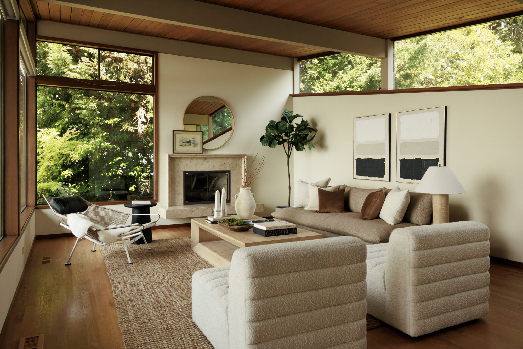 Seattle's best commercial food and hospitality photographer A modern living room with large windows, a beige sofa, two white armchairs, and a light wood coffee table, beautifully captured by a Seattle commercial interior design photographer for restaurants and hotels. Lush green trees are visible outside. captured by seattle's best food and lifestyle photographer Brooke Fitts