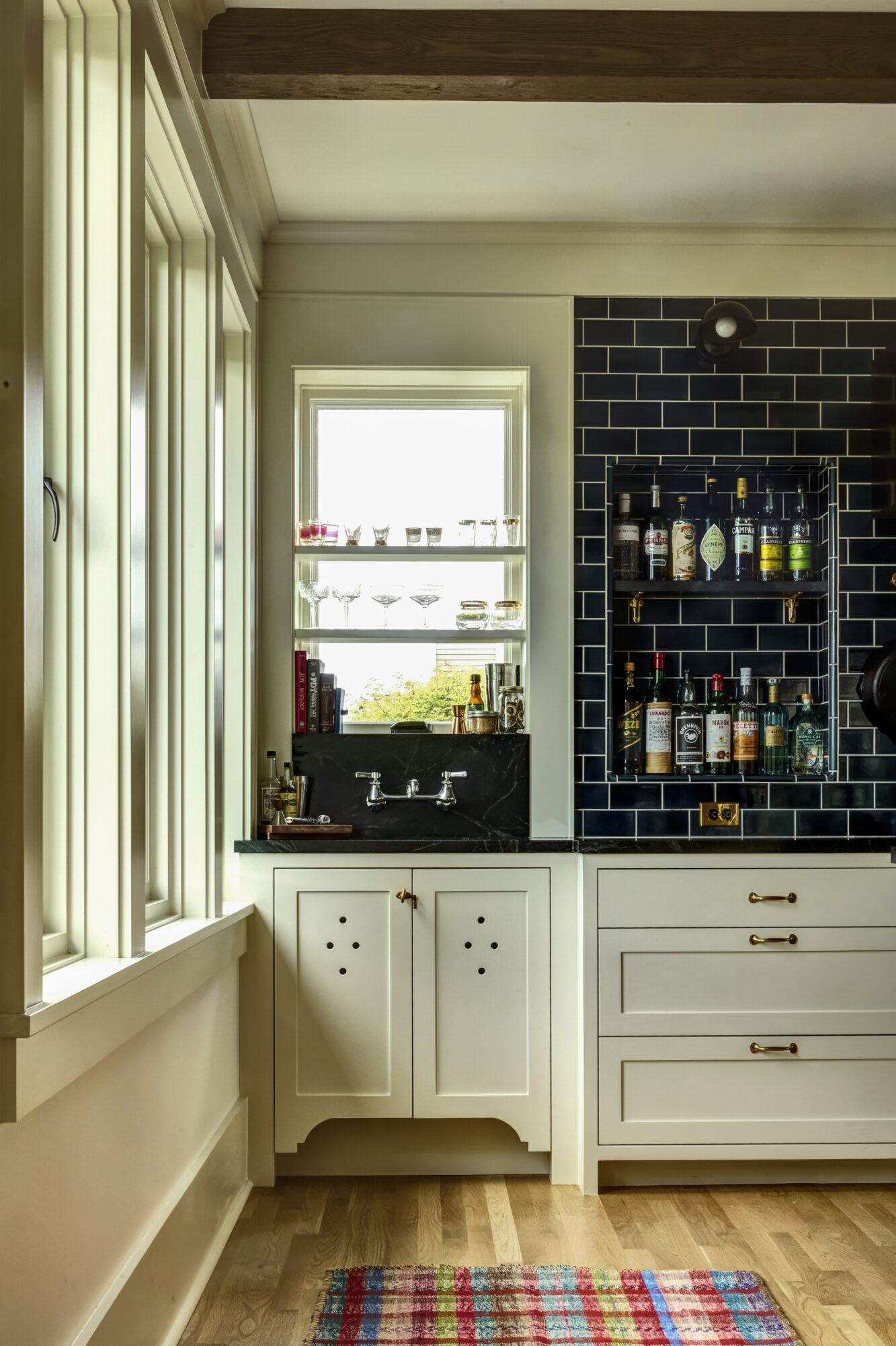 Seattle's best commercial food and hospitality photographer A cozy home bar area, beautifully captured by a Seattle commercial interior design photographer for restaurants and hotels, features a black tile backsplash, marble countertop, shelves with spirits and glassware, white cabinets, and a colorful rug on warm wooden floors. captured by seattle's best food and lifestyle photographer Brooke Fitts