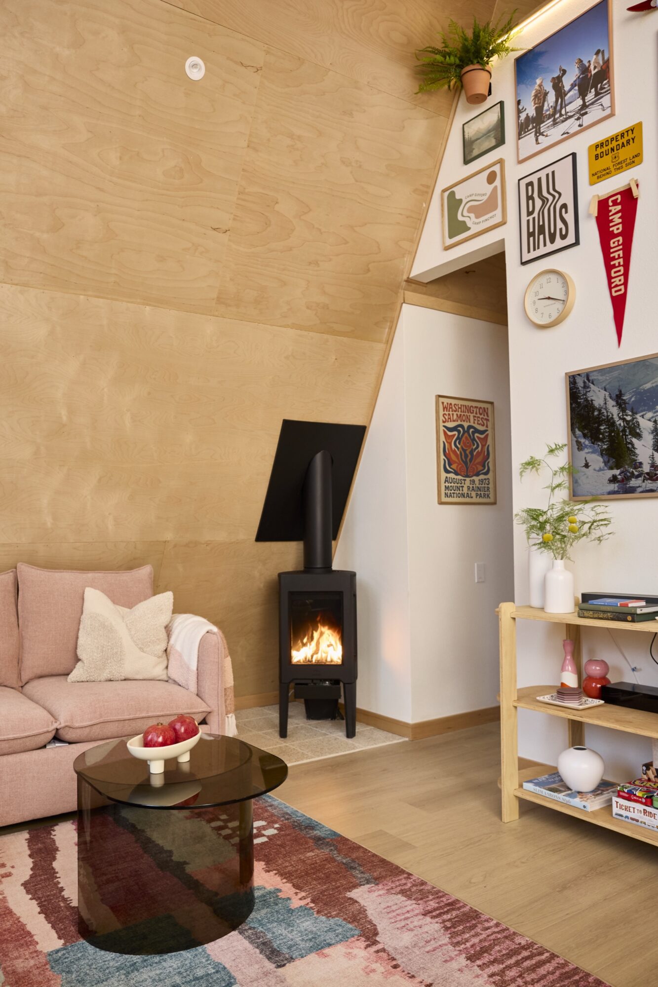Seattle's best commercial food and hospitality photographer Cozy living room with a pink sofa, glass coffee table, colorful rug, and wood-burning stove. Captured by a Seattle commercial interior design photographer for restaurants and hotels, each detail glows in the warm, wooden interior with artful decor and inviting charm. captured by seattle's best food and lifestyle photographer Brooke Fitts