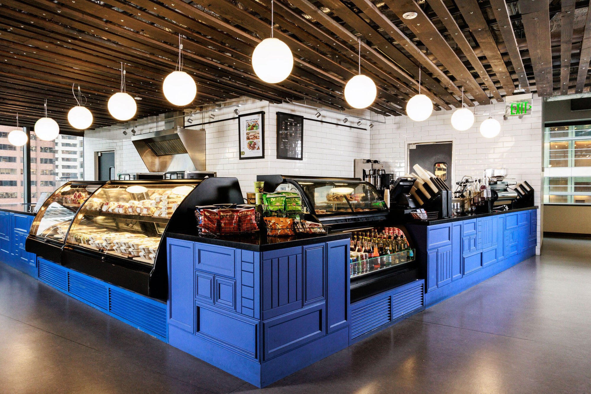 Seattle's best commercial food and hospitality photographer Modern café with blue counters, glass display cases filled with pastries and drinks, and snack bags on the counter—captured by a Seattle commercial interior design photographer for restaurants and hotels. Large windows flood the wood-paneled space with natural light. captured by seattle's best food and lifestyle photographer Brooke Fitts