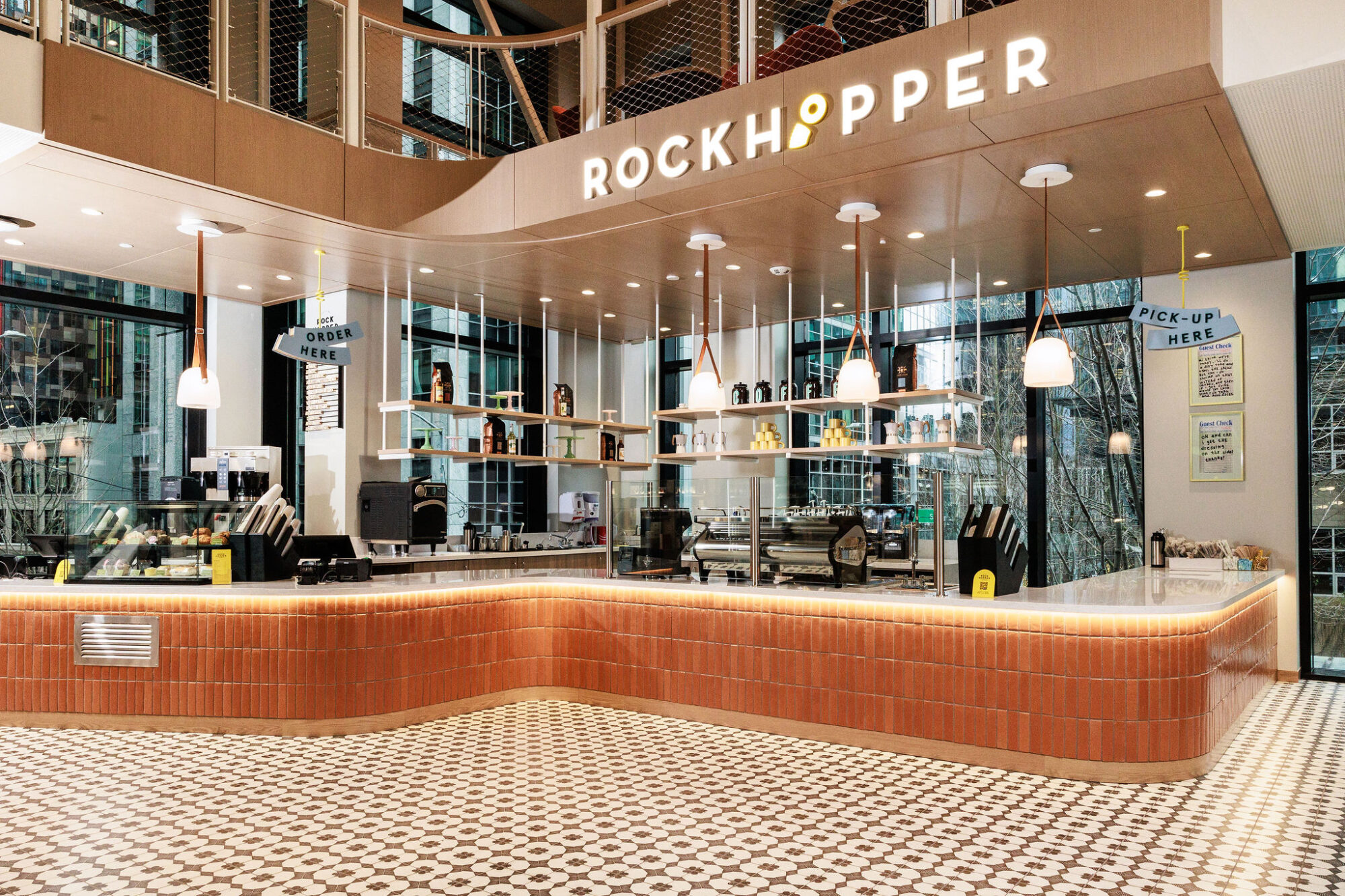 Seattle's best commercial food and hospitality photographer A modern café named Rockhopper with a tiled floor, curved counter, hanging lights, and shelves with drinks and snacks—captured by a Seattle commercial interior design photographer for restaurants and hotels. Large windows fill the space with natural light. captured by seattle's best food and lifestyle photographer Brooke Fitts