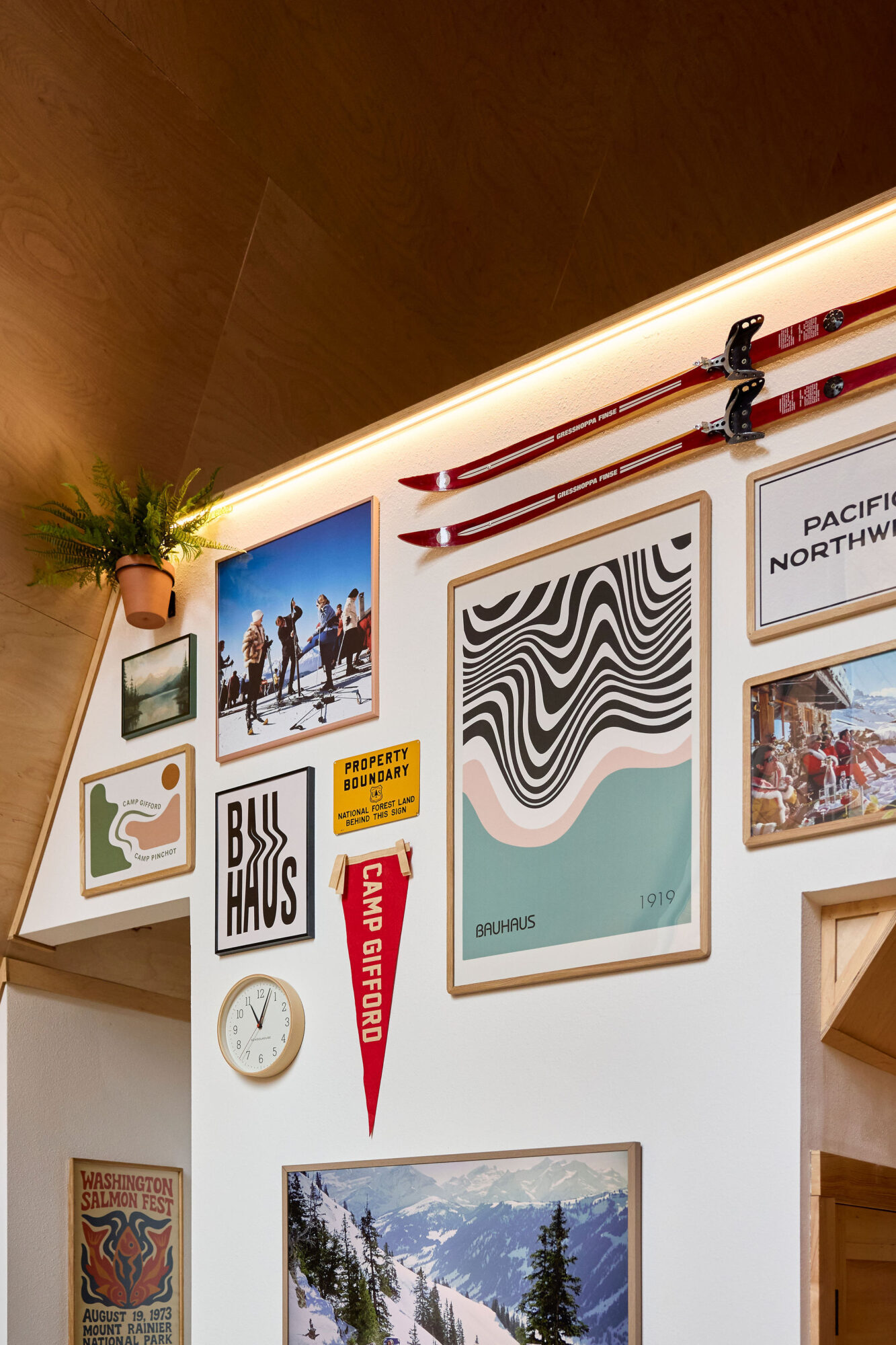 Seattle's best commercial food and hospitality photographer A wall decorated with vintage ski gear, photos, Bauhaus posters, a Camp Gifford pennant, and a potted plant on a wooden shelf—captured by a Seattle commercial interior design photographer for restaurants and hotels—with snowy peaks below. captured by seattle's best food and lifestyle photographer Brooke Fitts