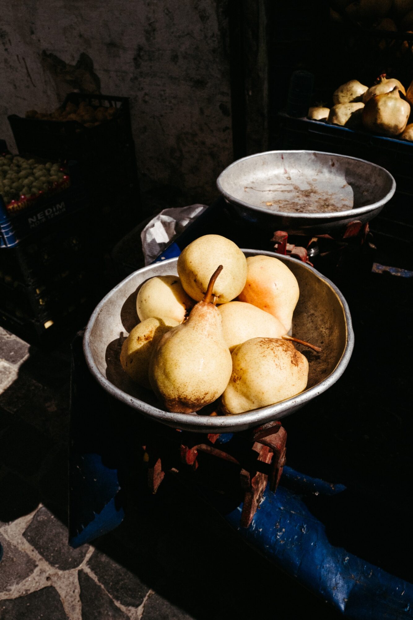 Seattle's best commercial food and hospitality photographer A metal bowl filled with ripe pears is placed on an old-fashioned weighing scale at an outdoor market, with sunlight casting shadows over the scene. captured by seattle's best food and lifestyle photographer Brooke Fitts