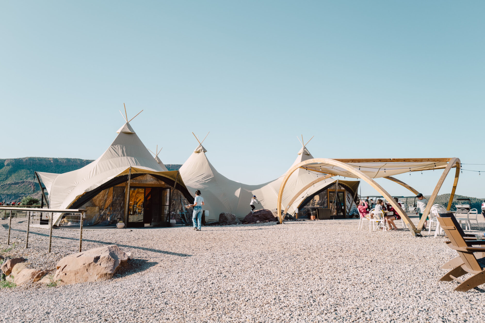 Seattle's best commercial food and hospitality photographer Three large beige tents with wooden frames stand on a gravel area under a clear sky, with people walking and sitting nearby; mountains are visible in the background. captured by seattle's best food and lifestyle photographer Brooke Fitts
